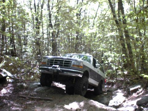 1995 Ford Bronco - This two-tone Ford Bronco navigates a challenging rocky path through a dense forest.