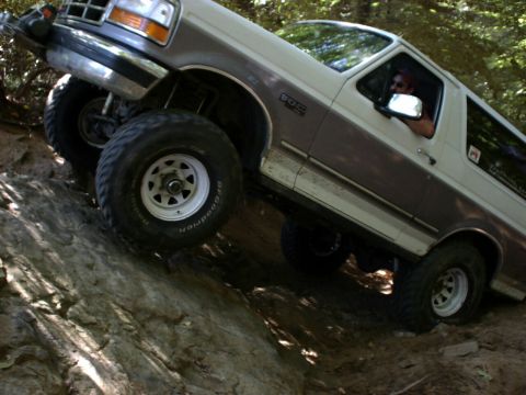 1995 Ford Bronco - A two-tone Ford Bronco navigates a challenging rocky trail, its off-road capabilities.