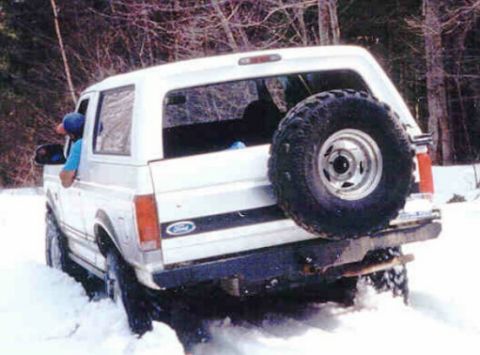 1995 Ford Bronco - A white 1995 Ford Bronco navigates through a snowy terrain, showing its rear profile and spare tire.
