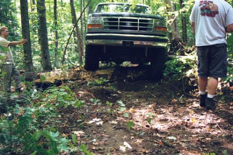 1995 Ford Bronco - A 1995 Ford Bronco navigates a wooded trail with two people observing.