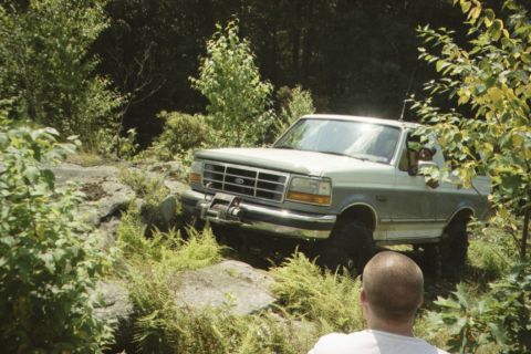 1995 Ford Bronco - A gray Ford Bronco navigates a challenging rocky path surrounded by lush greenery.