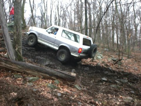 1995 Ford Bronco - A 1995 Ford Bronco navigates a steep, muddy trail through a forest.