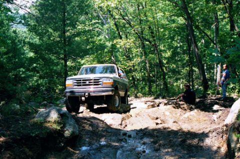 1995 Ford Bronco - A Ford Bronco navigates a challenging off-road course through a wooded area.