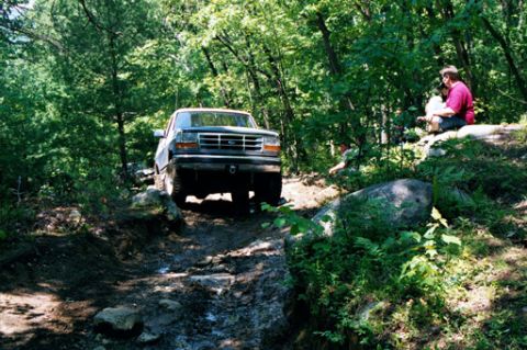 1995 Ford Bronco - Ford Bronco navigates a challenging off-road path through the woods.