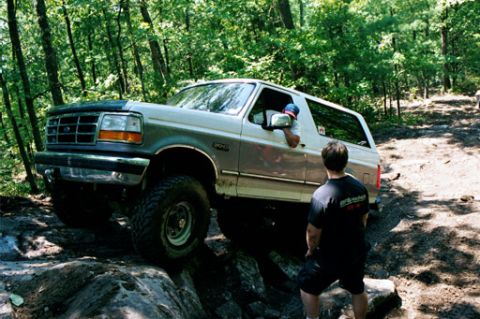 1995 Ford Bronco - A 1995 Ford Bronco tackles a challenging off-road trail with a person watching.