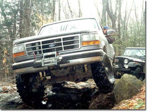 1995 Ford Bronco - A 1995 Ford Bronco tackles a challenging off-road course with another vehicle visible in the background.