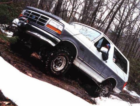 1995 Ford Bronco - This two-tone Ford Bronco navigates a challenging off-road path with snow and mud.