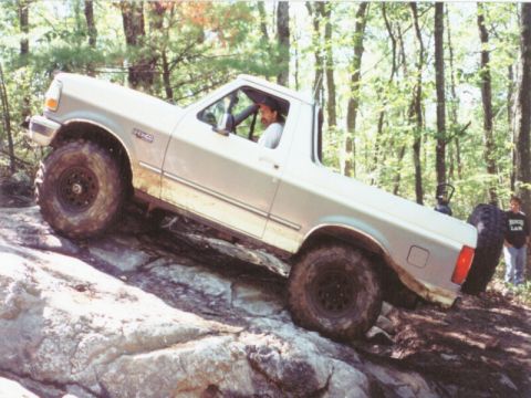 1995 Ford Bronco - A silver Ford Bronco navigates a rocky trail in a wooded area.