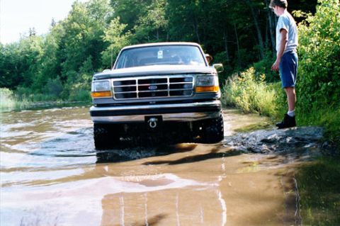 1995 Ford Bronco - A 1995 Ford Bronco navigates a shallow water crossing on a sunny day.