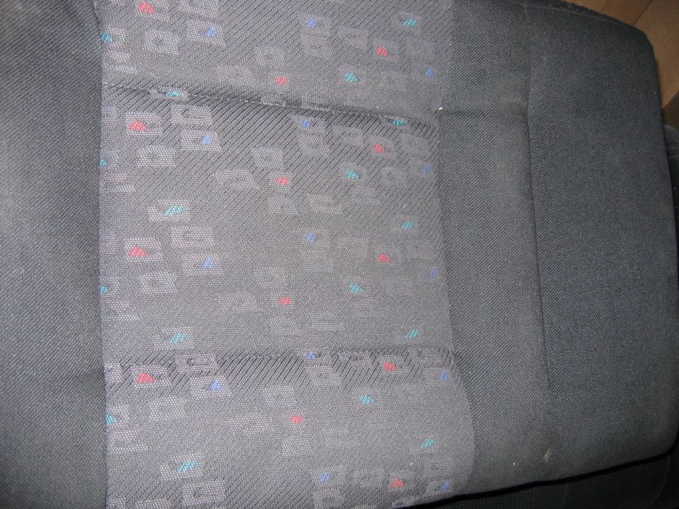 Close-up of gray car seat fabric with a repeating geometric pattern of red, blue, and teal squares