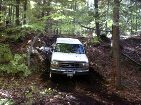 1995 Ford Bronco - A white 1995 Ford Bronco navigates a wooded off-road trail, kicking up dirt.