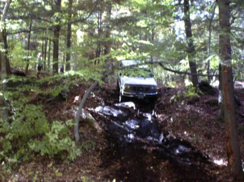 1995 Ford Bronco - This 1995 Ford Bronco navigates a challenging muddy trail in a forest setting.