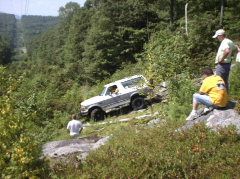 1995 Ford Bronco - A white Ford Bronco navigates a challenging off-road course with spectators observing the action.