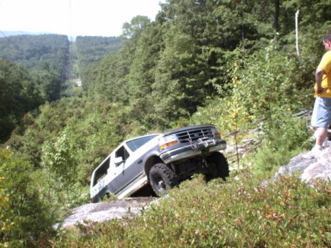 1995 Ford Bronco - A 1995 Ford Bronco navigates a steep, rocky incline surrounded by dense foliage.