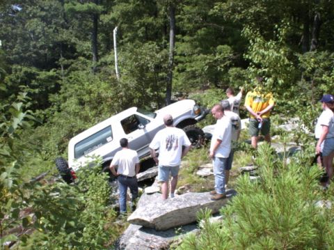 1995 Ford Bronco - A group of people observe a white 1995 Ford Bronco that has become stuck on a steep, rocky terrain.
