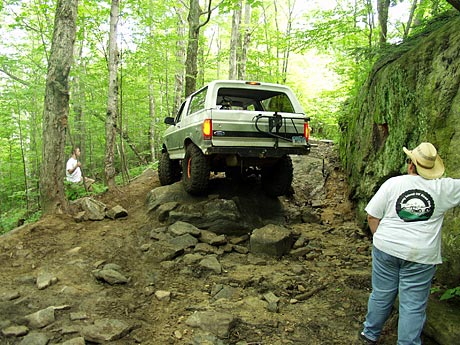 1995 Ford Bronco - A lifted Ford Bronco navigates a challenging rocky path through a dense forest.