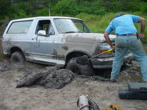 1995 Ford Bronco - A man attempts to free a mud-covered Ford Bronco from a deep mire.