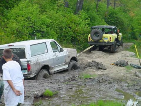 1995 Ford Bronco - A white 1995 Ford Bronco is stuck in the mud, with a yellow Jeep assisting with a tow strap.
