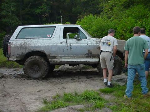 1995 Ford Bronco - A muddy white Ford Bronco is stuck in the dirt with people standing nearby.