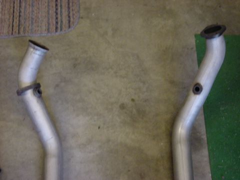 1989 Ford Bronco - Two exhaust pipes are shown on a concrete floor with a carpeted area in the background.