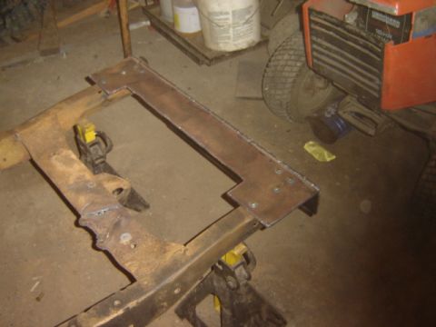1992 Ford Bronco - A vehicle frame is being modified with welded metal plates while supported by yellow jack stands in a garage.