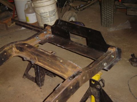 1992 Ford Bronco - A vehicle frame is supported by jack stands in a workshop environment.