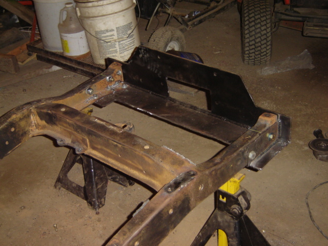 Rusty vehicle frame on yellow jack stands with black metal brackets welded on
