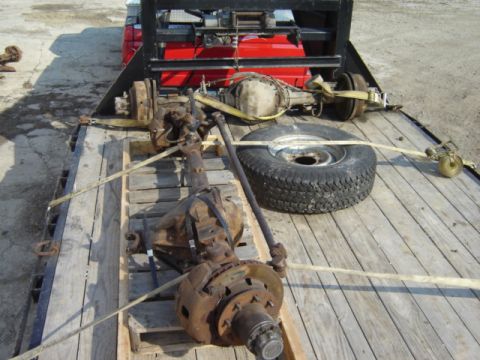 1992 Ford Bronco - Vehicle axles and a spare tire are being transported on a flatbed trailer, secured with straps.