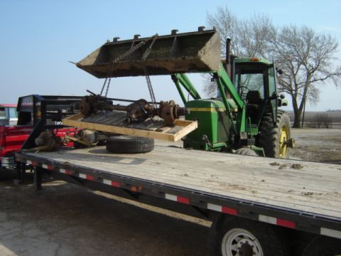 1992 Ford Bronco - A tractor is used to move axles from a flatbed trailer in an outdoor setting.