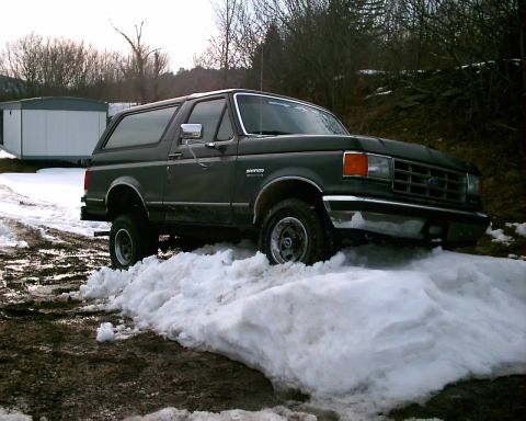 1988 Ford Bronco - A dark green Ford Bronco navigates a snowy path, its front end angled towards the viewer.