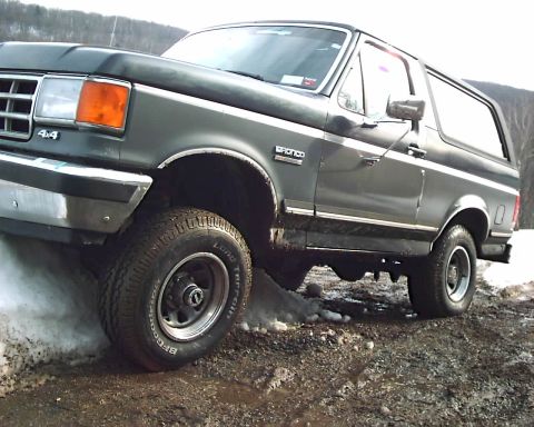 1988 Ford Bronco - This Ford Bronco is navigating a rough, off-road terrain with patches of snow and mud.