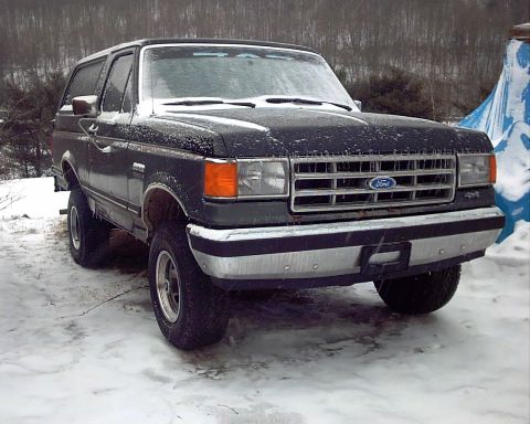 1988 Ford Bronco - A dark Ford Bronco sits in the snow, its grille and headlights visible.