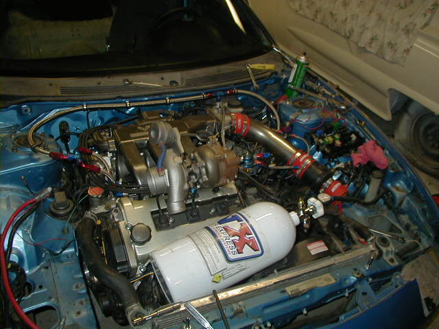 Engine bay with turbocharger, intercooler piping, and a white nitrous oxide tank. Blue paint on the engine bay walls