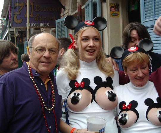 Man in purple shirt with beads, woman in Mickey Mouse ears and sweater, and another woman in Mickey Mouse ears and sweater on Bourbon Street