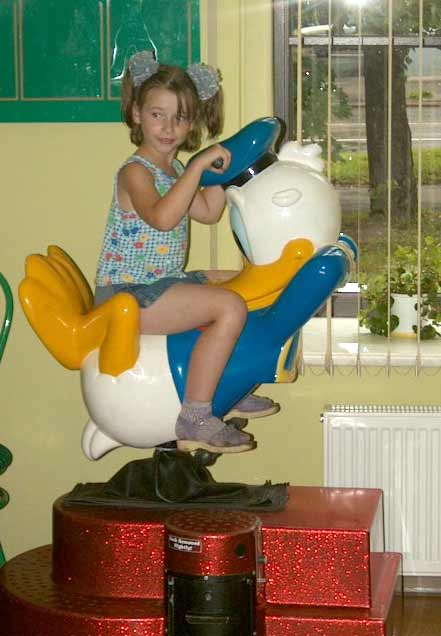 1968 Ford Mustang - A young girl in a floral tank top and denim shorts sits on a coin-operated kiddie ride shaped like a white and yellow cartoon duck, mounted…