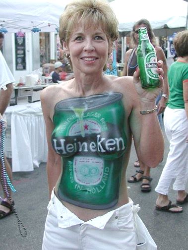 1968 Ford Mustang - A woman at an outdoor street festival poses holding a green Heineken bottle, with a Heineken beer-can design painted on her torso as body a…