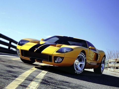 1985 Ford Bronco - A yellow sports car with black racing stripes is shown driving on a road under a clear blue sky.