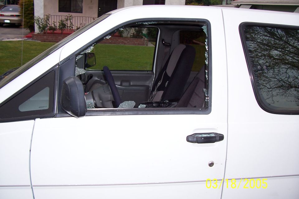 White van with broken driver's side window and shattered glass on the interior