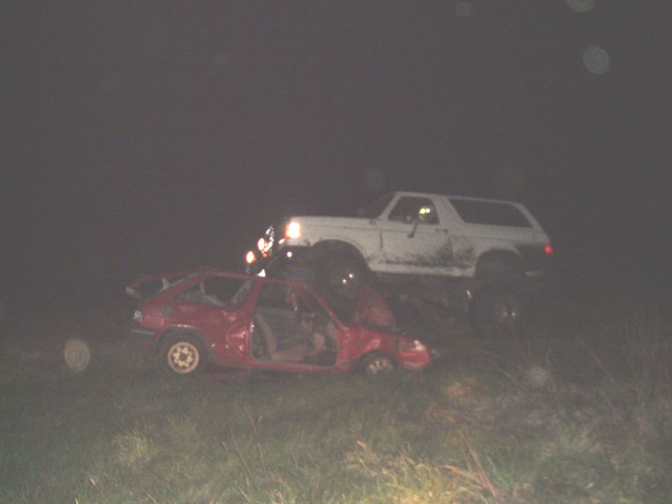 1989 Ford Bronco on top of a wrecked red car at night