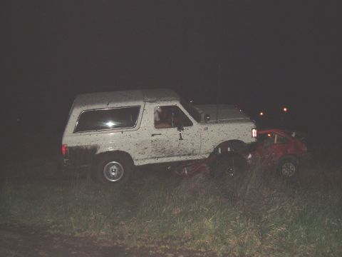 1989 Ford Bronco - A white 1989 Ford Bronco is seen on top of a red car in this nighttime scene.
