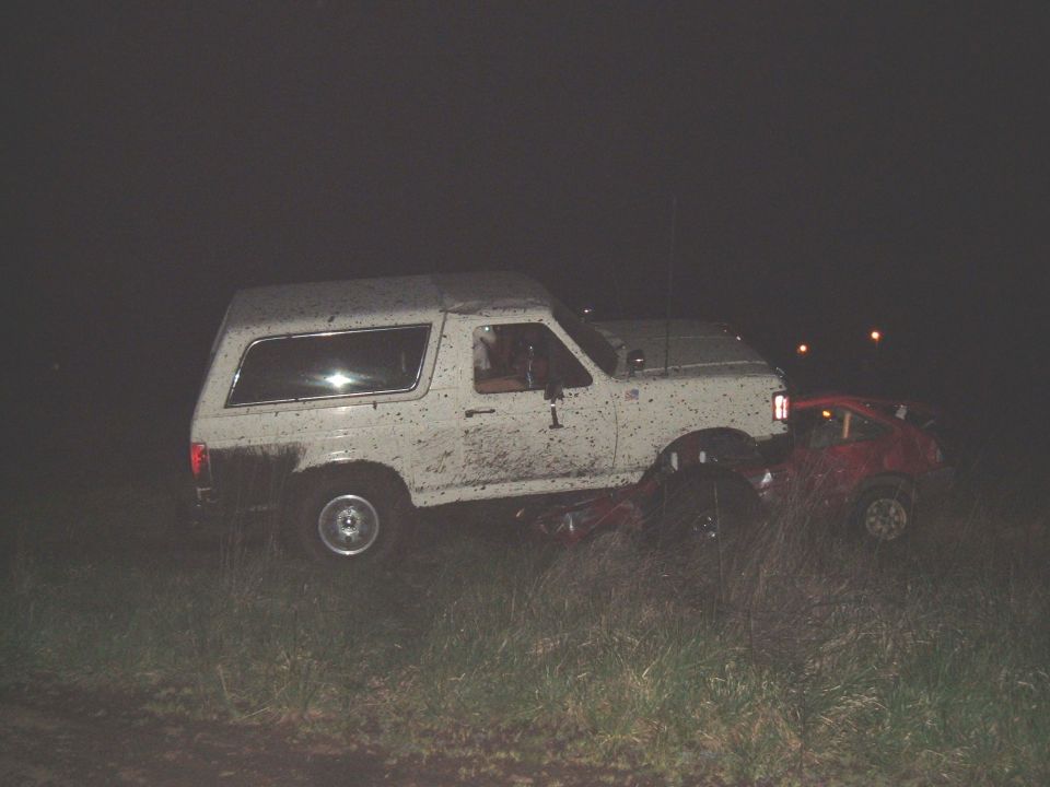 White 1989 Ford Bronco on top of a red car at night