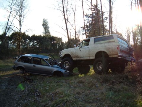 1989 Ford Bronco - A lifted Ford Bronco appears to have driven over a wrecked Honda Civic in a wooded area.