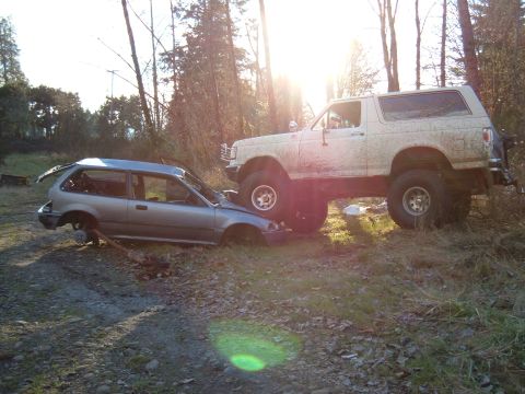 1989 Ford Bronco - A lifted Bronco appears to be crushing a heavily damaged Honda Civic in an outdoor setting.