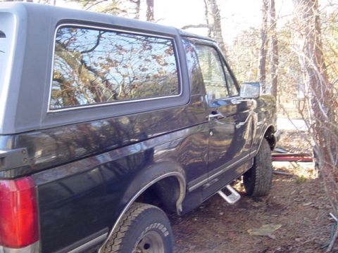 1989 Ford Bronco - A black Ford Bronco is parked outdoors, with trees reflected in its windows.