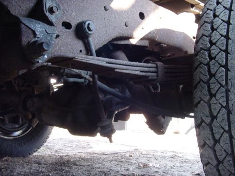 1989 Ford Bronco - Close-up of the rear axle and suspension system of a vehicle, showing leaf springs and a tire.