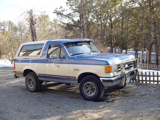 1989 Ford Bronco parked on gravel with trees and snow in background