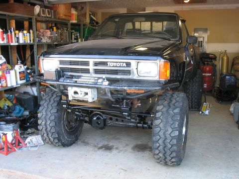 1986 Ford F-150 - Front view of a modified black Toyota pickup truck with off-road tires and a winch, inside a cluttered garage.