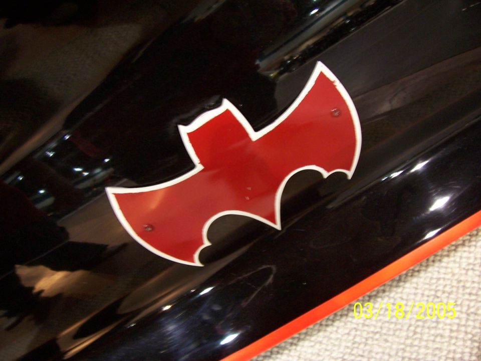 Black car panel with a red and white bat symbol emblem. Orange trim visible