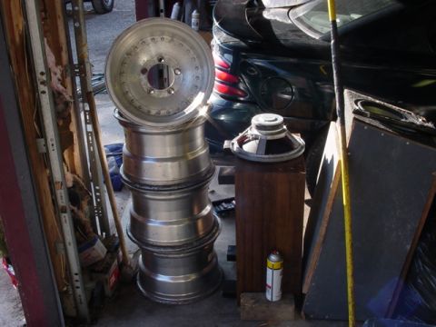 1989 Ford Bronco - A stack of aluminum wheels and car speakers are visible in a garage setting, with a dark colored car in the background.