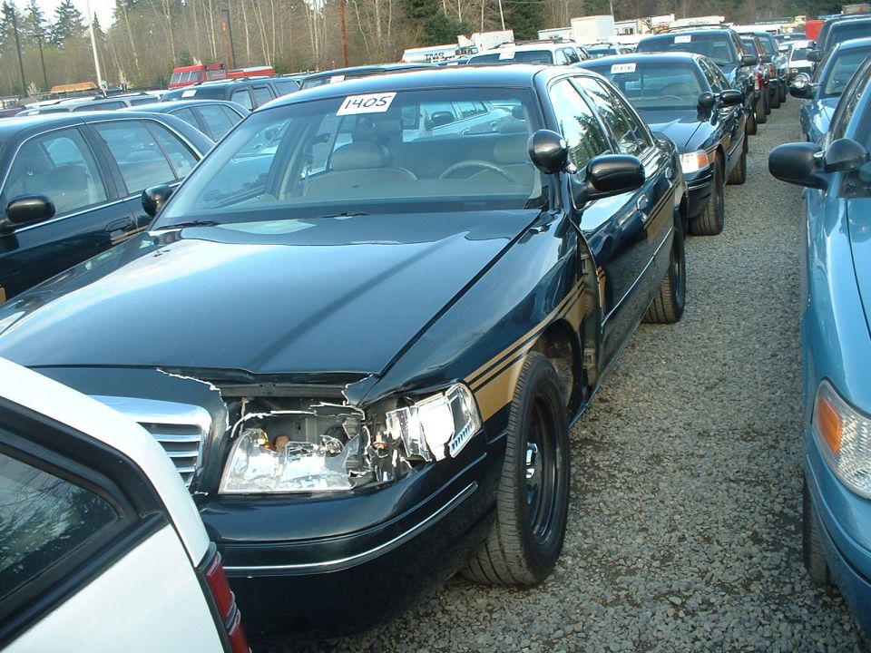 Dark sedan with gold stripe, damaged headlight and hood, parked in a lot with other vehicles